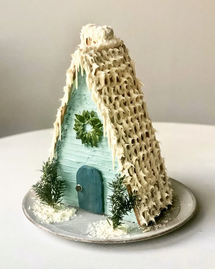 a small house made out of straw with a door and wreath on the roof is sitting on a plate