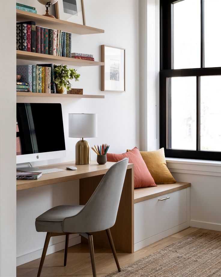 a desk with a computer, chair and bookshelf in front of a window