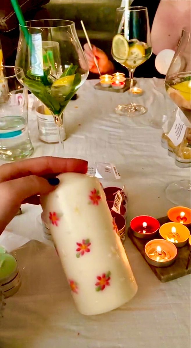 a person is holding a candle at a table with many glasses and candles on it