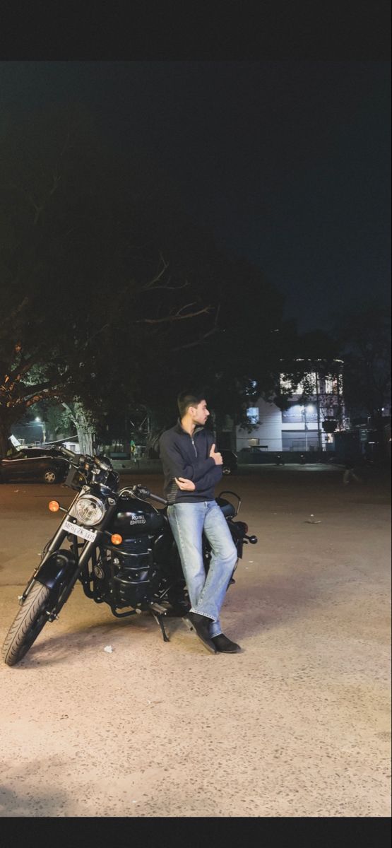 a man sitting on top of a motorcycle in the middle of a parking lot at night