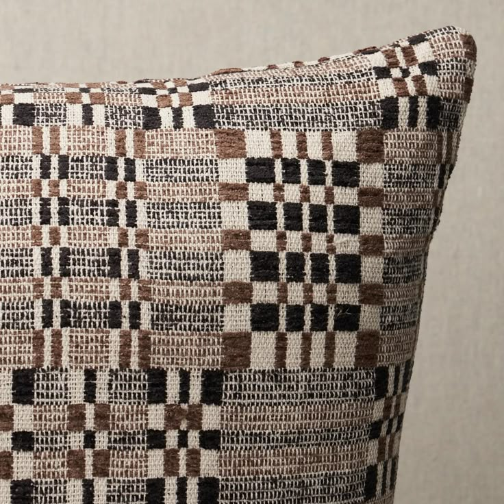 a brown and white checkered pillow sitting on top of a wooden table next to a wall