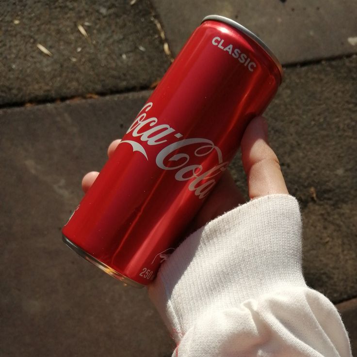 a person holding a can of coca - cola in their hand on the sidewalk,