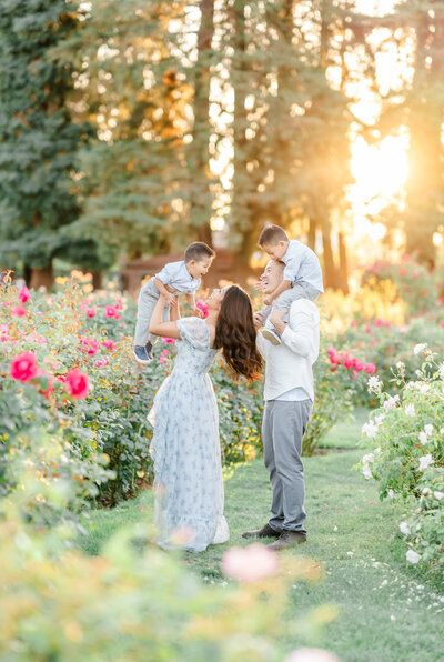 a man and woman holding their son in the middle of a flower garden at sunset