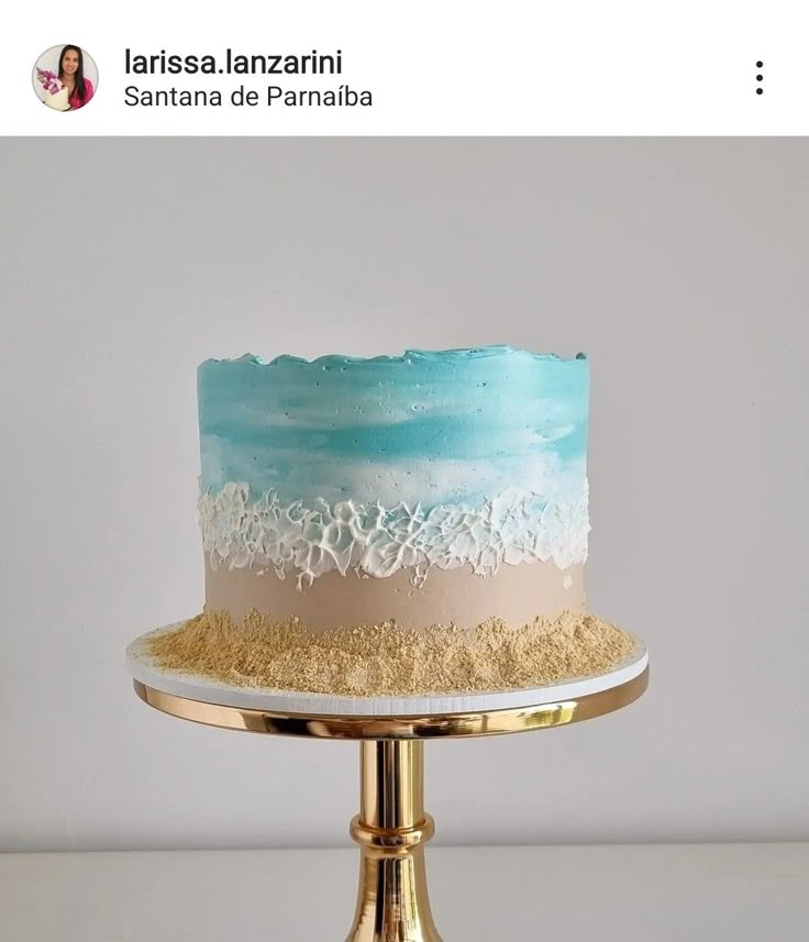 a blue and white cake sitting on top of a gold plate with sand around it