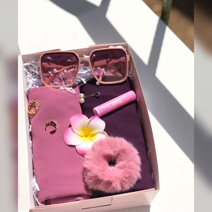 an open pink box with sunglasses and other items in it sitting on a table next to a flower