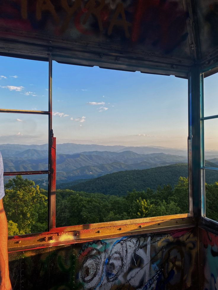 a man standing in front of a window looking out at the mountains and valleys below