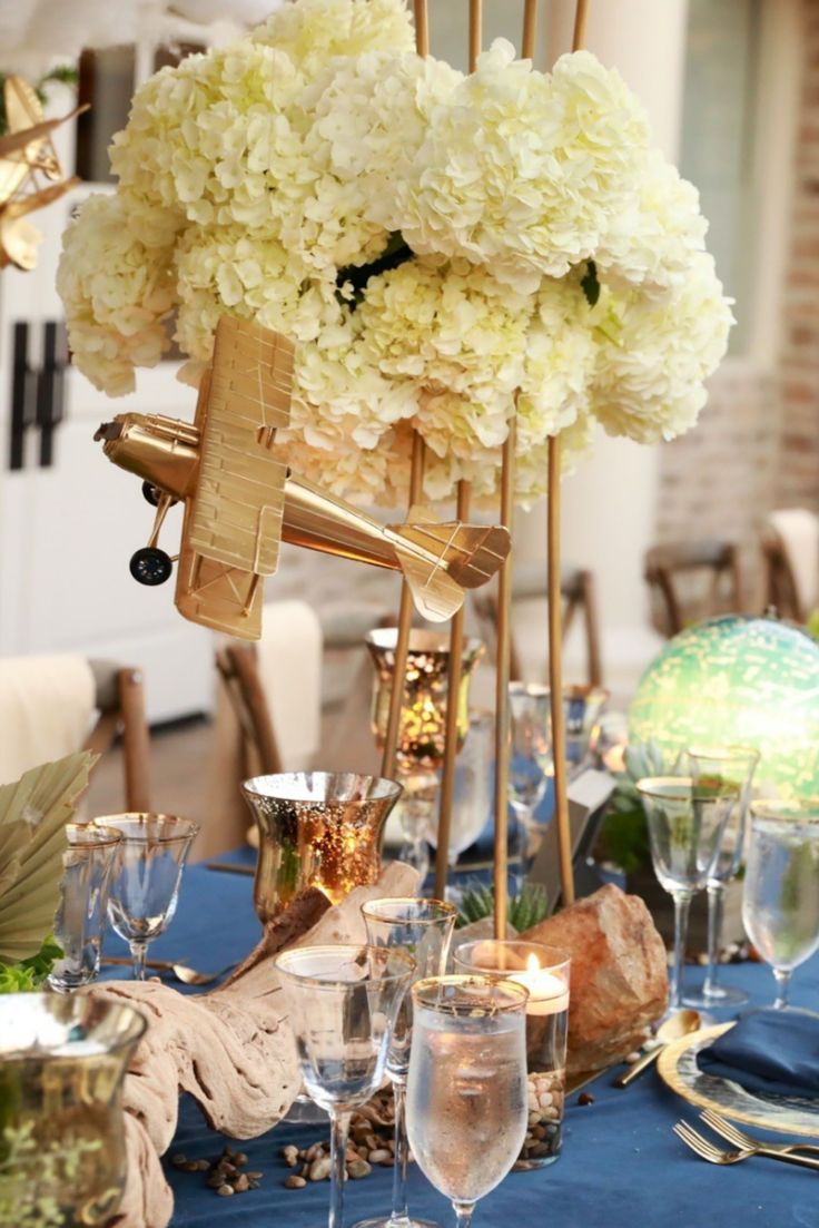 an arrangement of flowers and wine glasses on a blue table cloth with gold chargers around it