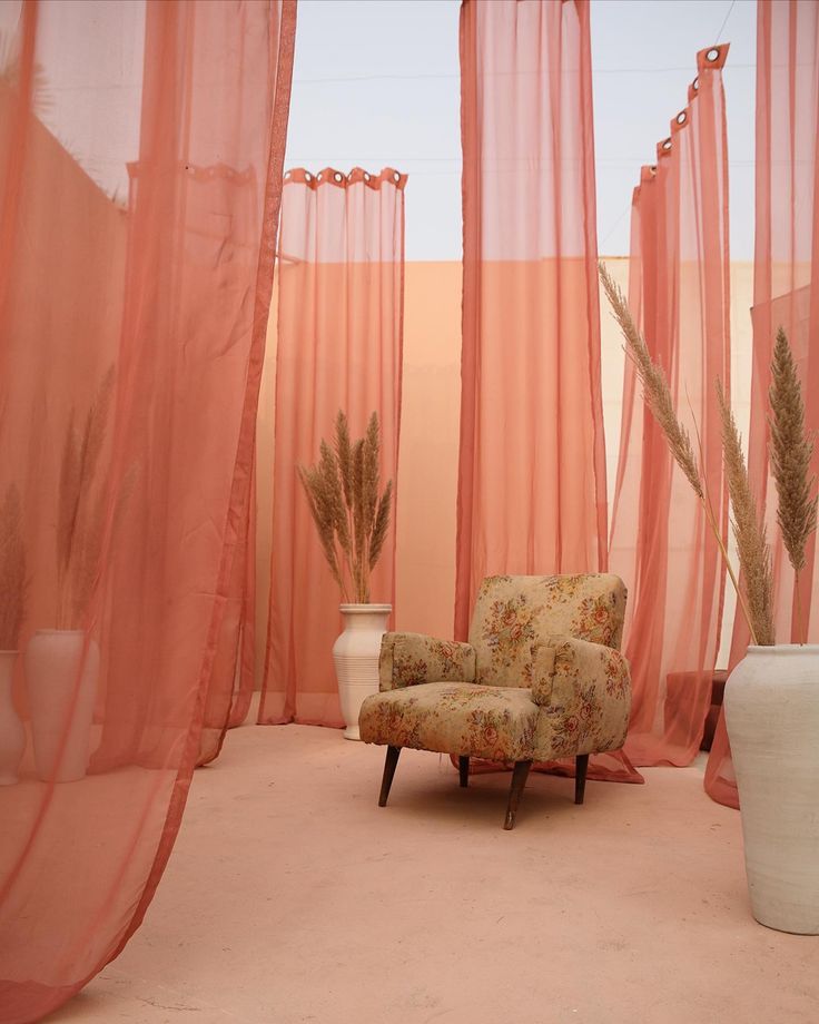 a chair sitting in front of sheer curtains and vases on the floor next to it