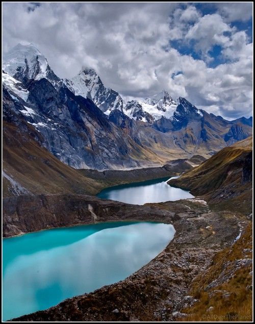 there is a blue lake in the middle of this mountain range with snow capped mountains behind it