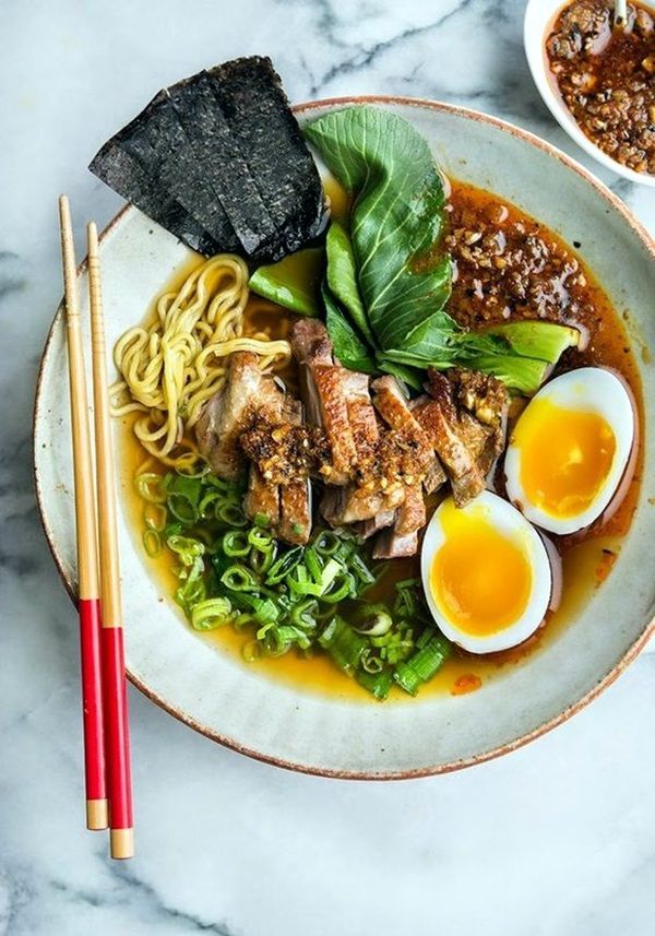 a bowl filled with noodles, meat and vegetables next to chopsticks