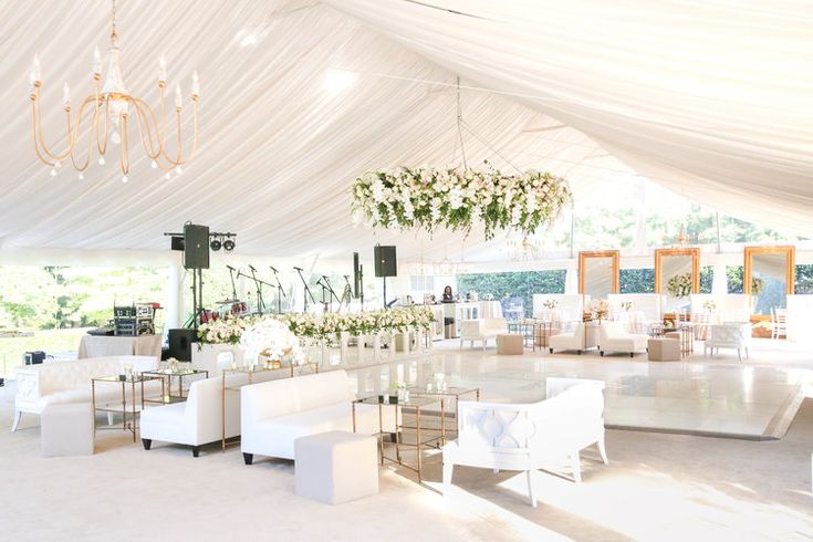 a large white tent with tables and chairs in front of it, surrounded by chandeliers