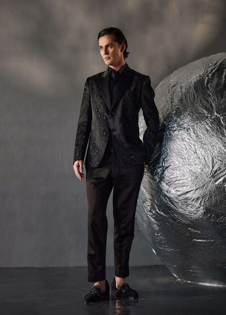 Editor's Note Featuring tone on tone embroidered dire black tux with kat dana details. Paired with a black pintuck shirt and black tapered trousers. Fabric: Linen silk Color: Black Components: Tuxedo, shirt and trousers Occasion: Evening wear Fit: Regular Note: Product colour may slightly vary due to photographic lighting sources Care: Dry clean only About the Designer After establishing himself as the leading couturier in the industry of menswear, Jatin Malik went on to explore luxury footwear. Fitted Designer Formal Sets, Designer Fitted Formal Sets, Fitted Designer Sets For Formal Occasions, Designer Evening Suits For Festive Occasions, Designer Festive Evening Suits, Designer Black Blazer With Pressed Crease, Tailored Evening Party Wear Suits, Luxury Fitted Evening Sets, Luxury Fitted Evening Set