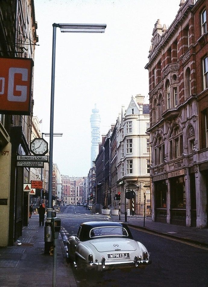 an old car is parked on the side of the road in front of tall buildings