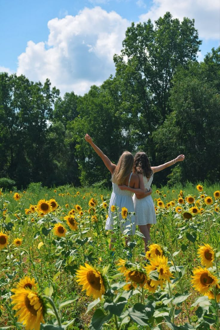 two girls are standing in the middle of a sunflower field with their arms outstretched