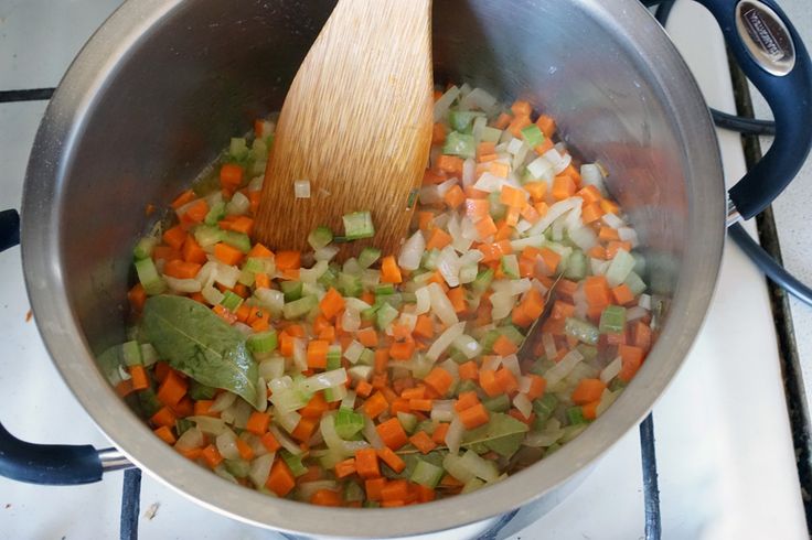 a pot full of chopped vegetables with a wooden spoon in it on the stove top