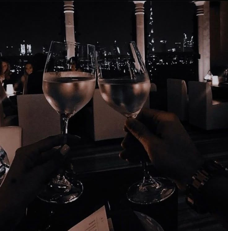 two people are toasting with wine glasses in front of the city skyline at night