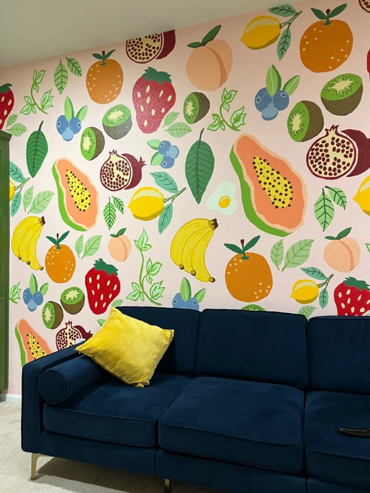 a blue couch sitting in front of a wall with fruit painted on it's walls