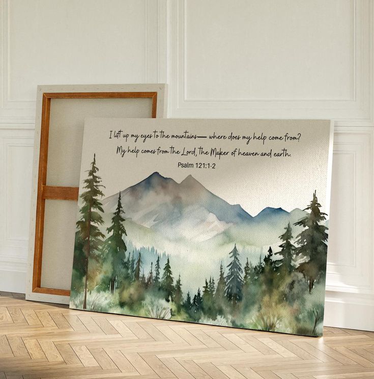 a painting on the floor next to a frame with an image of mountains and trees