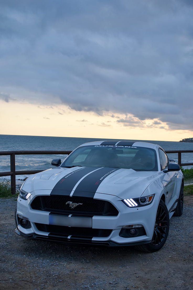 a white and black mustang parked on the beach