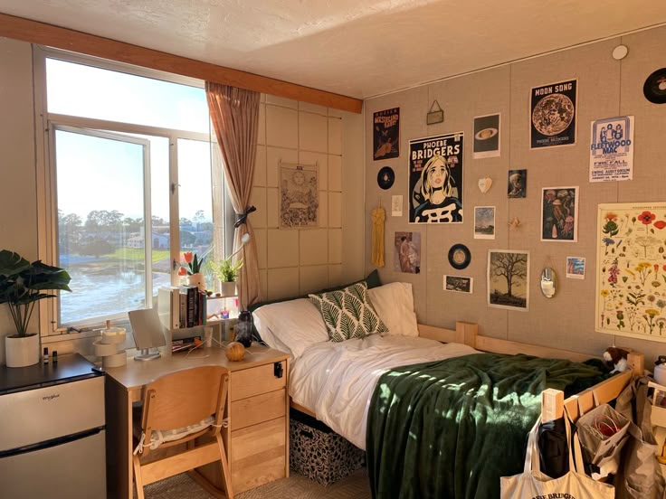 a dorm room with a bed, desk and small refrigerator freezer next to a window