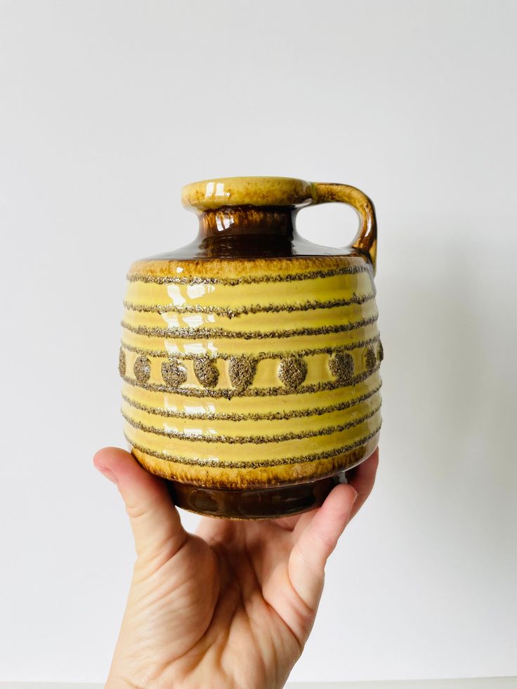 a hand holding a yellow and brown vase