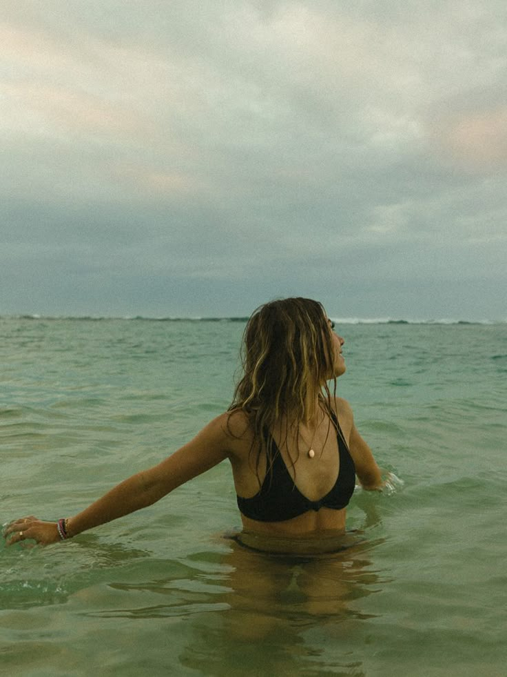 a woman standing in the ocean with her arms spread out and looking at the sky