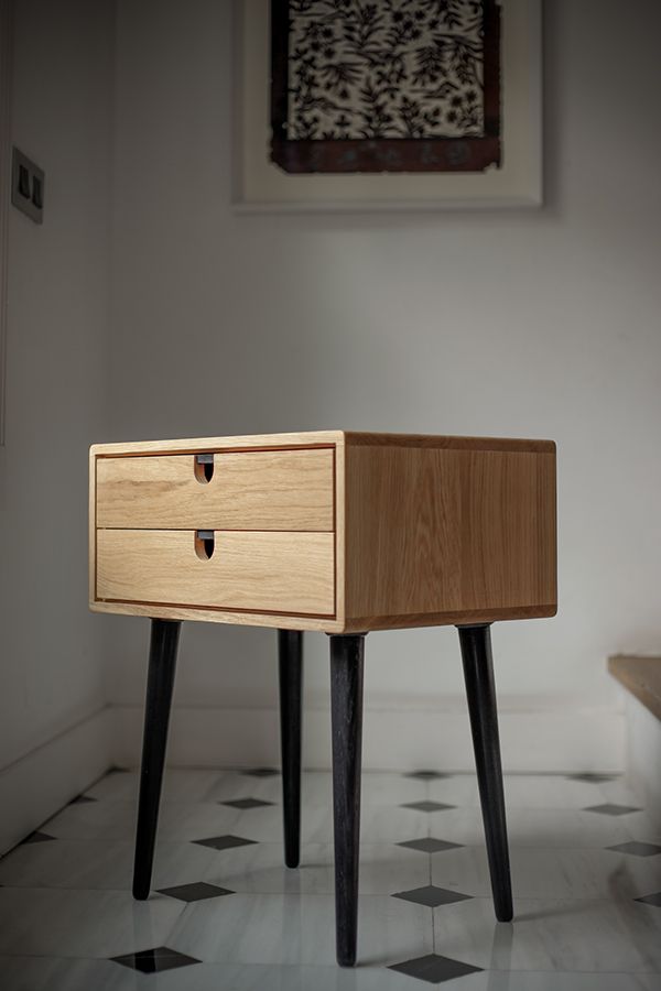 a small wooden table with two drawers on it's legs in a white room