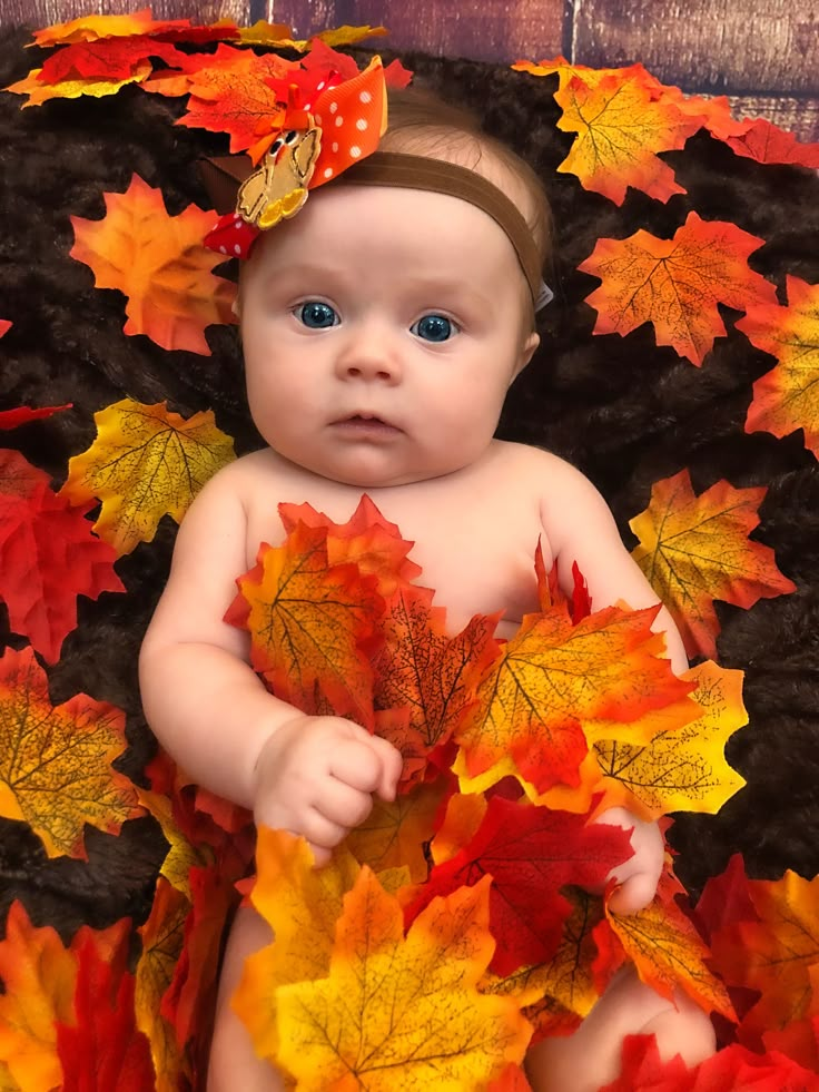 a baby is laying down with autumn leaves