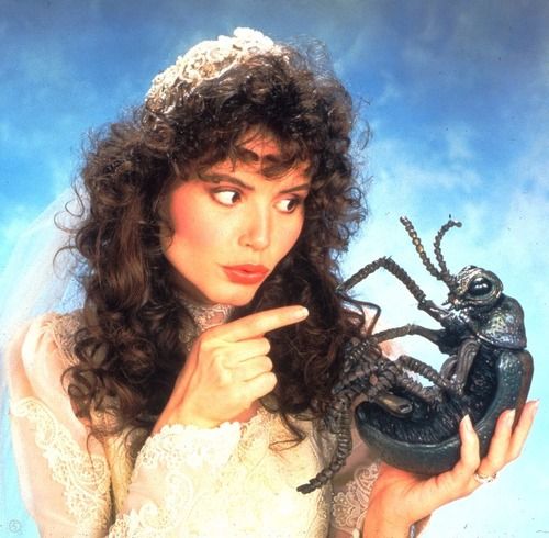 a woman in a white dress holding a black lizard and pointing to it's face