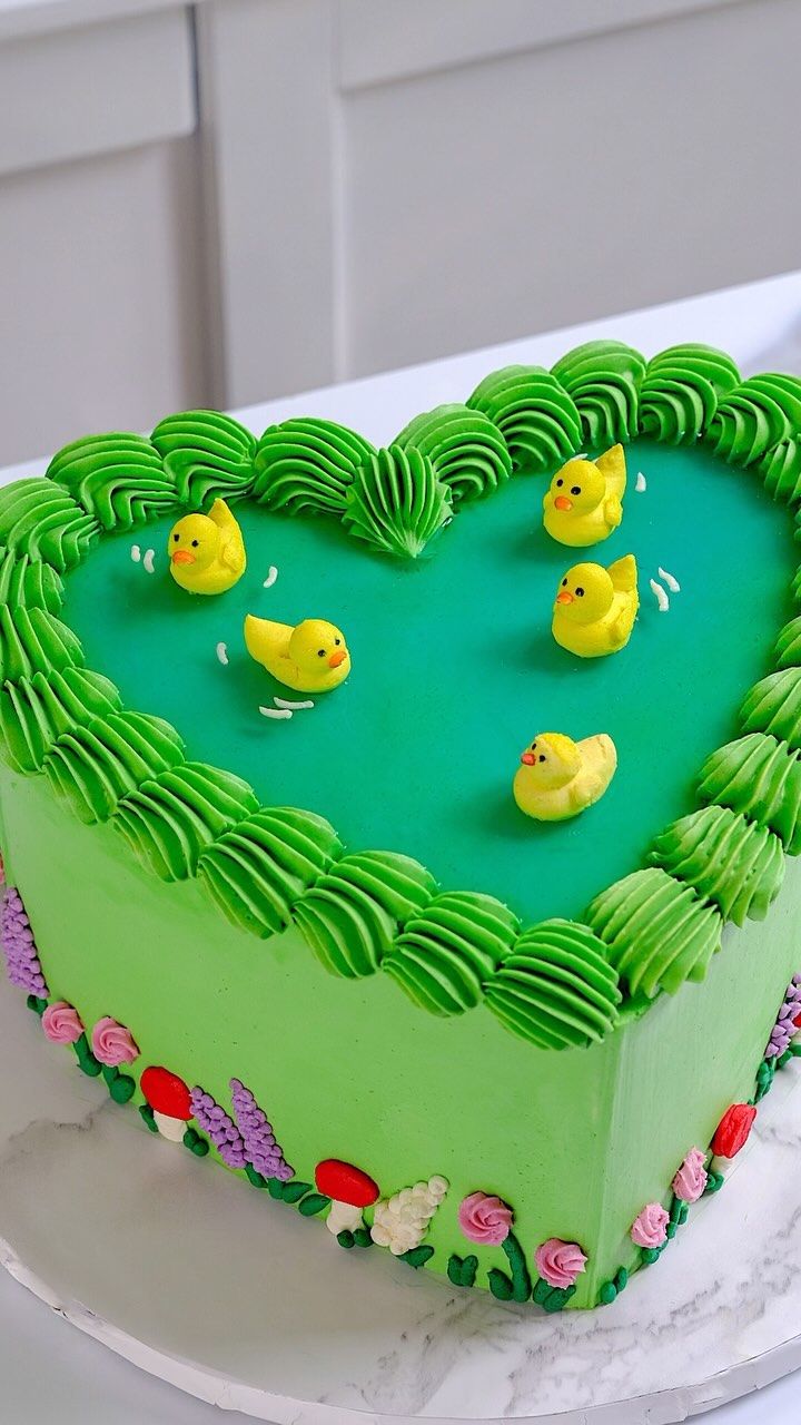 a heart shaped cake with ducks in the middle and green frosting, on a white plate