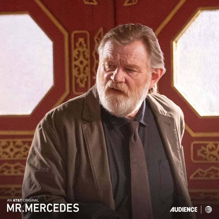 an older man wearing a suit and tie standing in front of a red door with the words mr mercedess on it