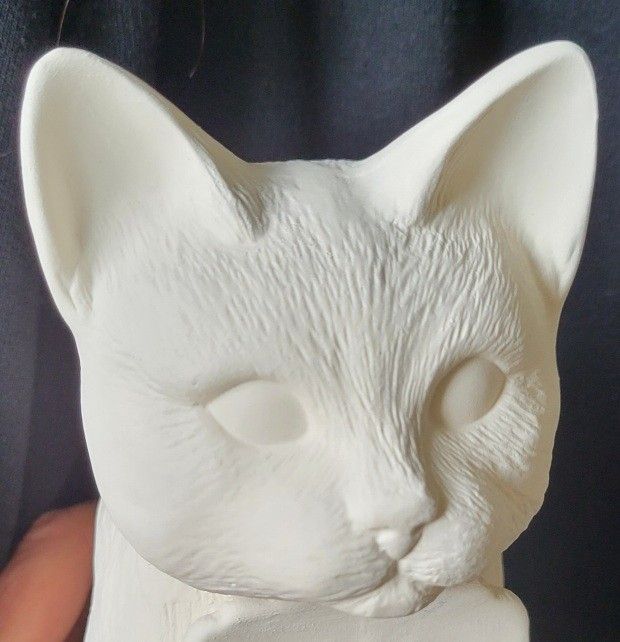 a white cat statue sitting on top of a black table next to a person's hand