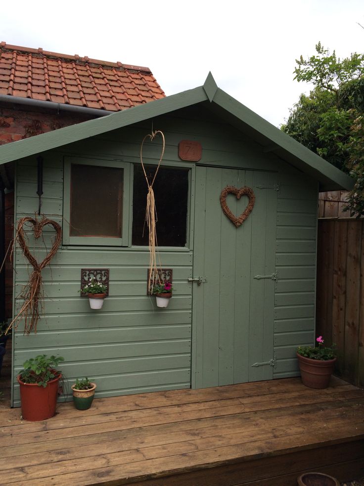 a small green shed with potted plants on the side and hearts hanging from the roof