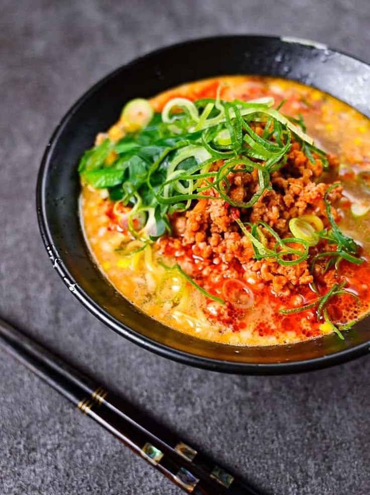 a black bowl filled with food next to chopsticks on top of a table