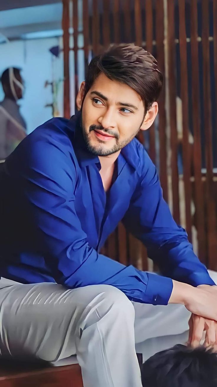 a man sitting on top of a wooden bench wearing a blue shirt and grey pants