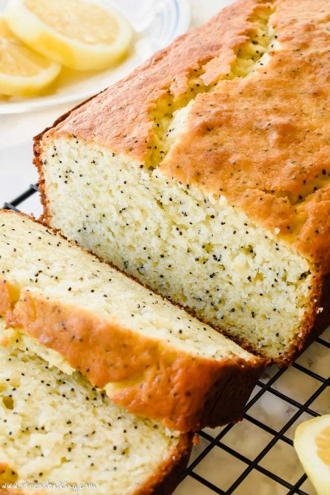 a loaf of lemon poppy seed bread on a cooling rack next to sliced lemons