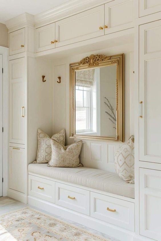 a bench with pillows and a mirror on it in a room filled with white cabinets