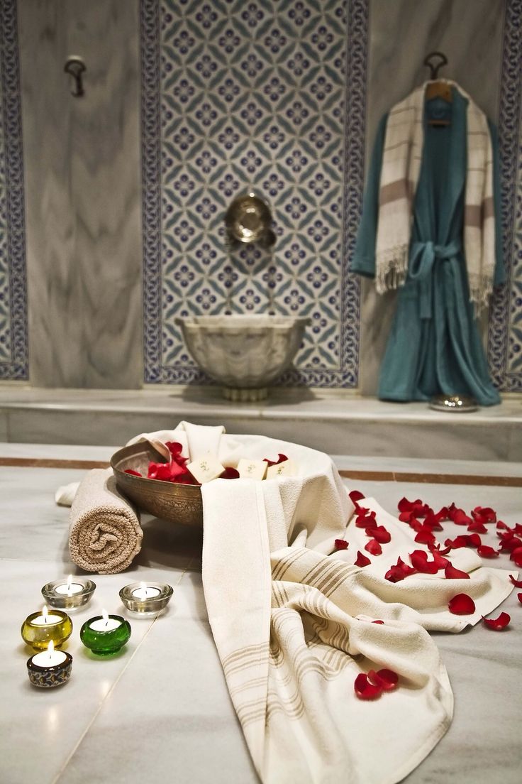 towels and candles on the floor in front of a bathtub with red rose petals