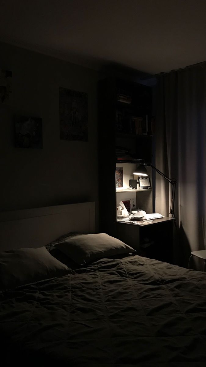 a dimly lit bedroom with a bed, desk and book shelf in the corner at night