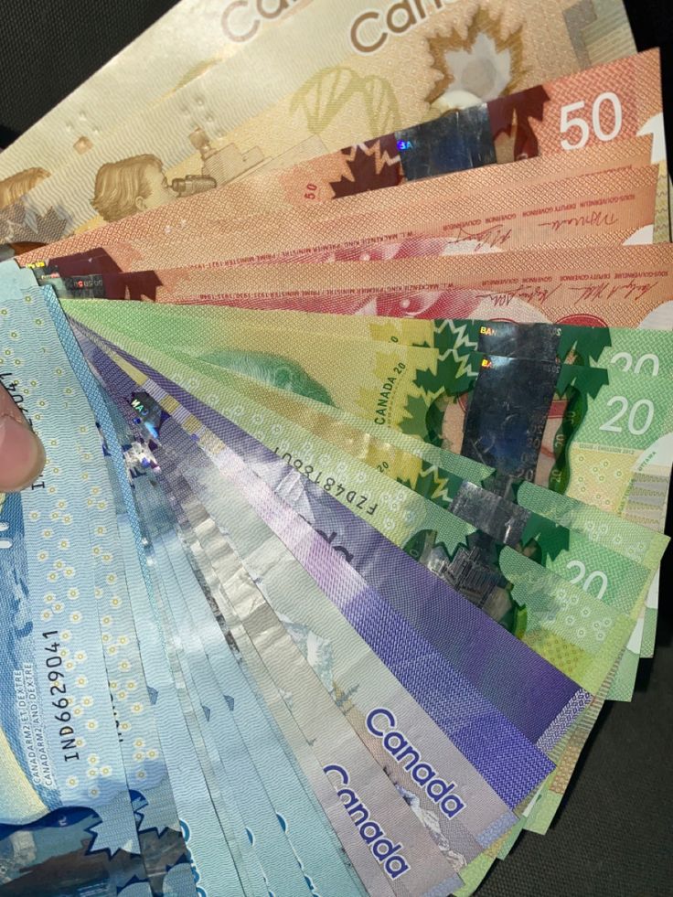 a person is holding several canadian money in one hand and the other on top of each other