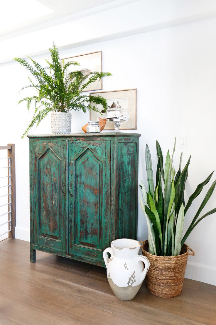 an old dresser is painted green and has pictures on the wall above it with plants