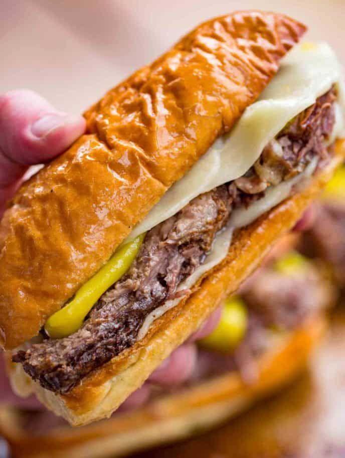 a close up of a person holding a sandwich in their hand with the words slow cooker italian beef on it