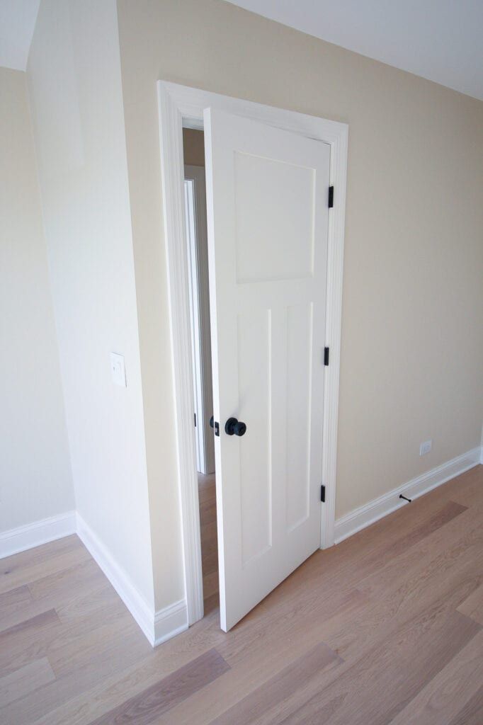 an empty room with white doors and hard wood flooring on either side of the door