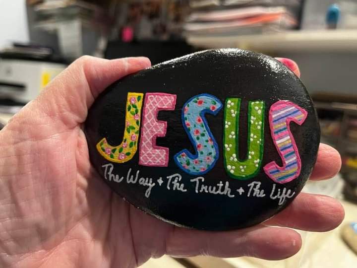 a hand holding a rock with the word jesus painted on it in different colors and designs