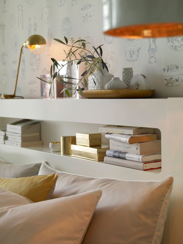 a bed with pillows and books on top of it next to a wall mounted shelf