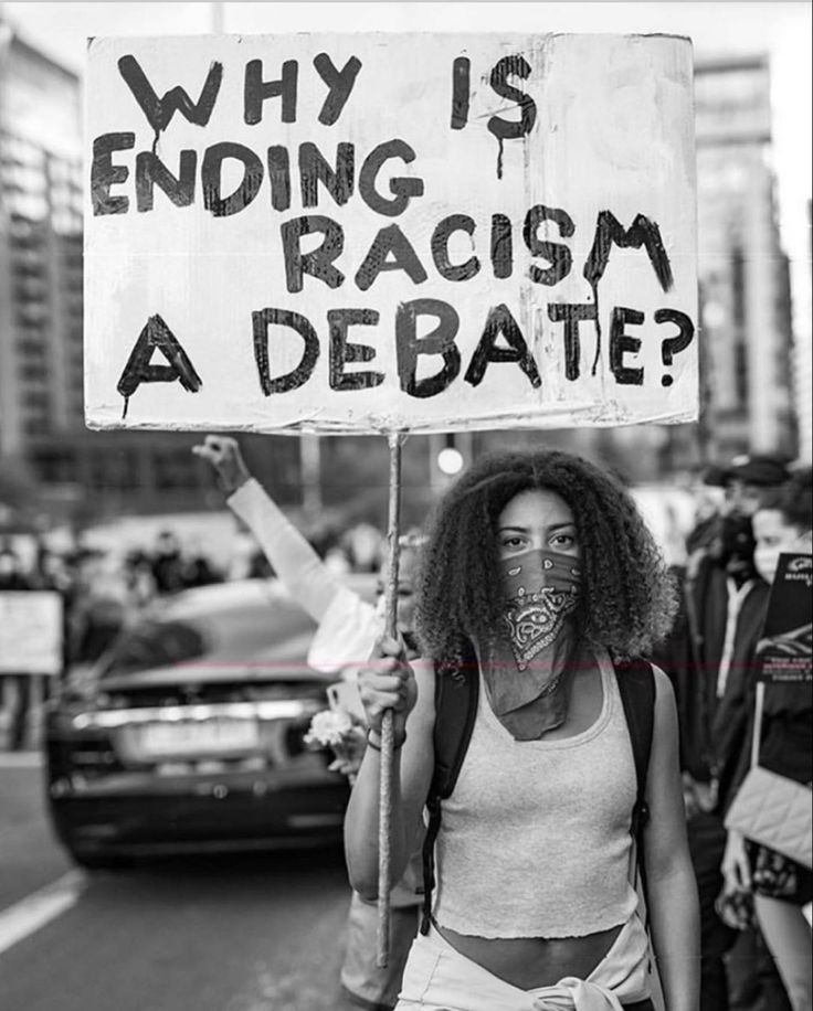 a woman holding a sign that says why is ending racism a debate?