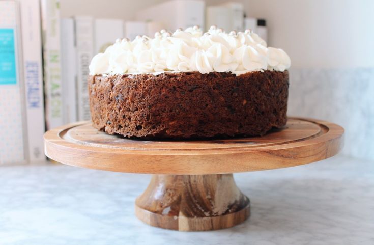 a chocolate cake with white frosting on a wooden platter next to some books