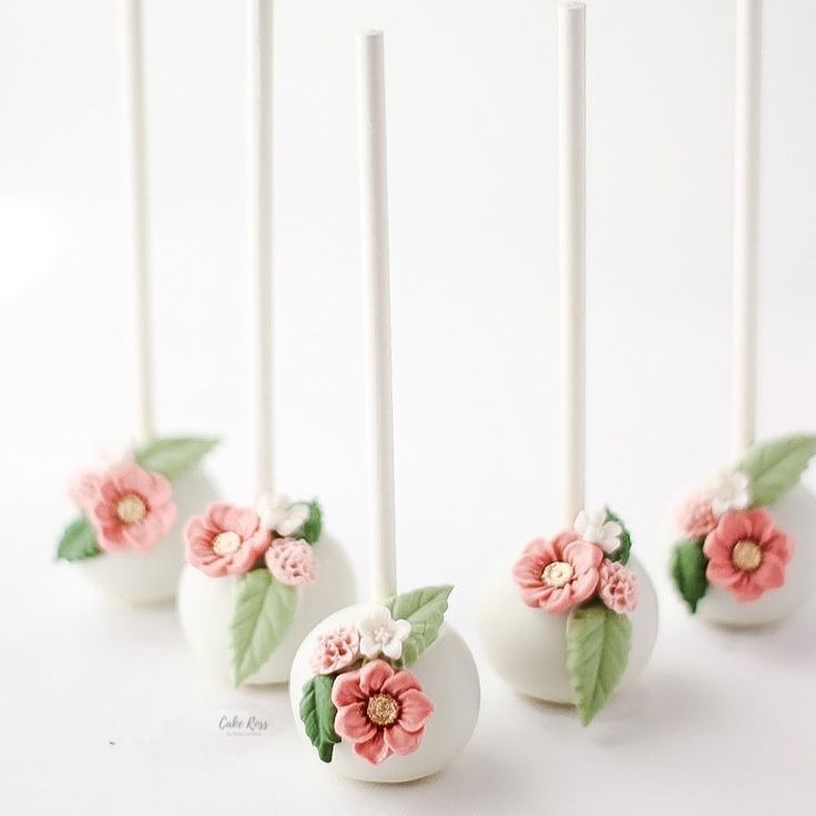 cake pops decorated with flowers and leaves are lined up on a white surface, ready to be eaten