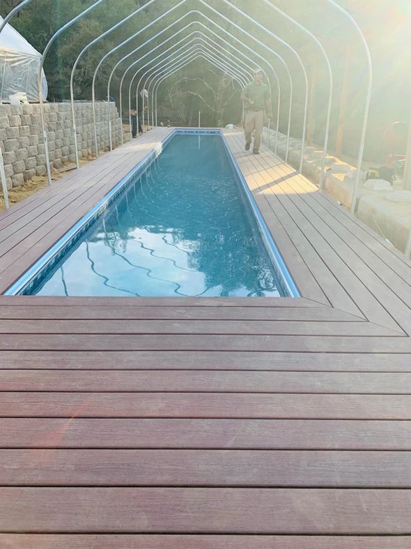 an empty swimming pool in the middle of a wooden decked area with glass walls