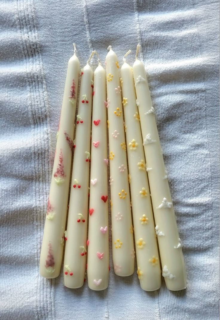 five white candles are lined up on a bed